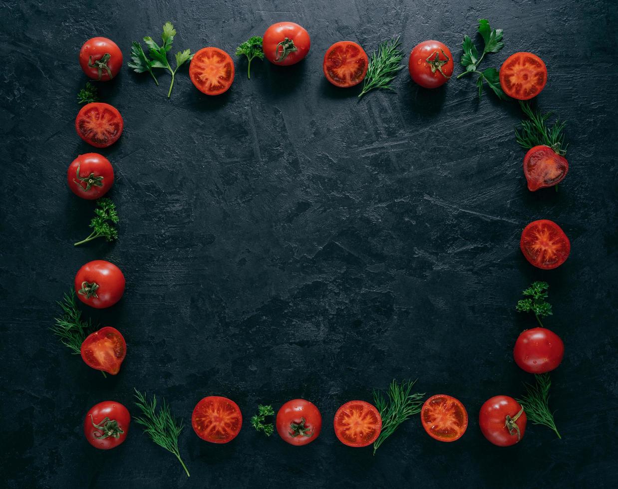 Composition of red tomatoes and green fresh parsley and dill lying on dark background in form of frame. Vegeterian food concept. Free space in middle photo