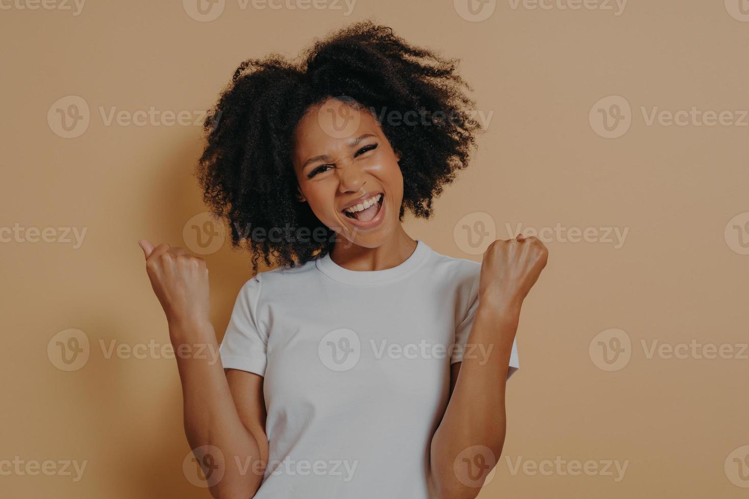 Young euphoric woman clenching fists and celebrating achievement, isolated on yellow background photo