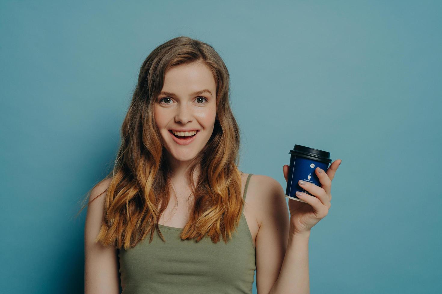 Joyful young girlish woman feeling carefree, holding disposable coffee cup and smiling at camera photo