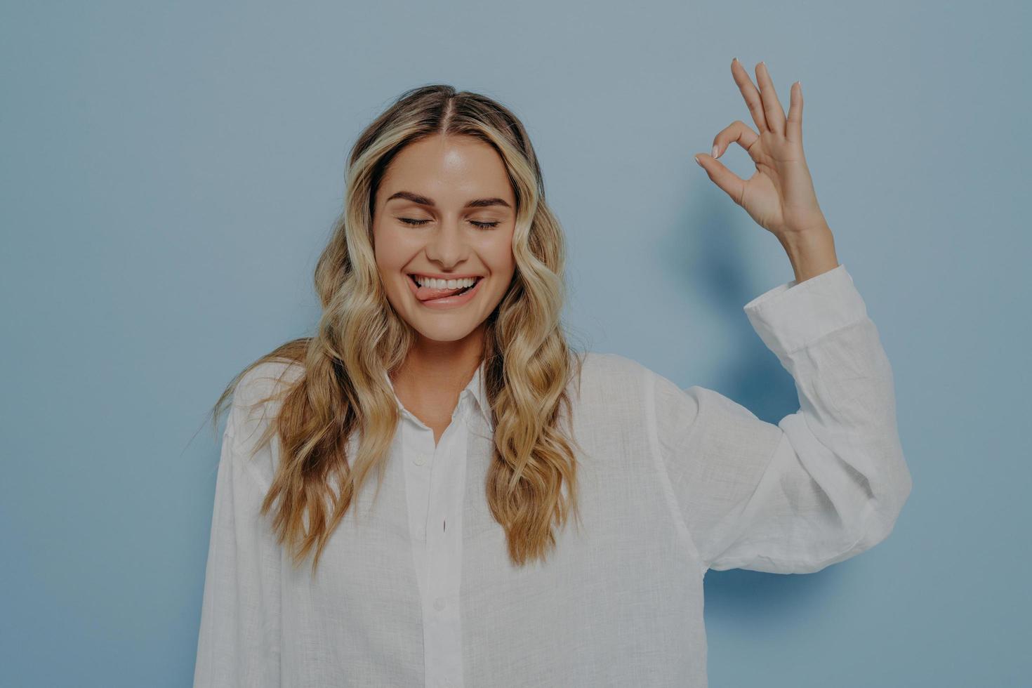 Crazy blonde woman making ok gesture while showing tongue photo