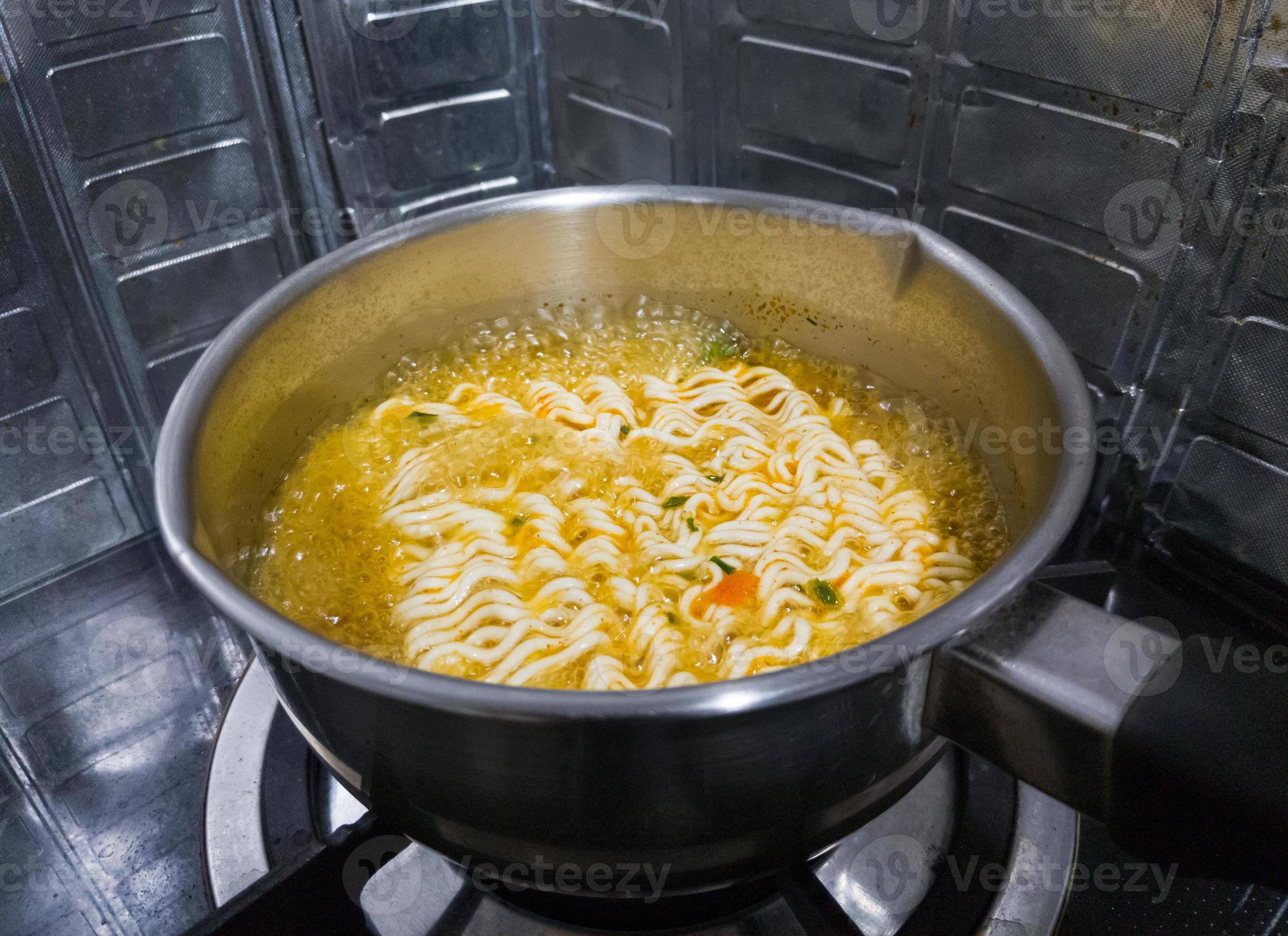 The spicy instant noodles are boiling in a metal pot on a gas stove