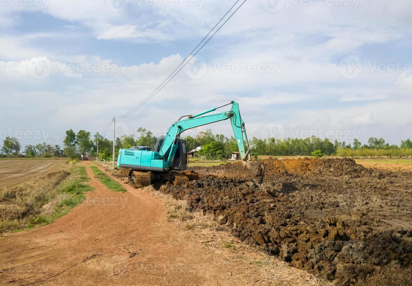Excavator is working on earthwork for digging the ponds near the paddy field. photo
