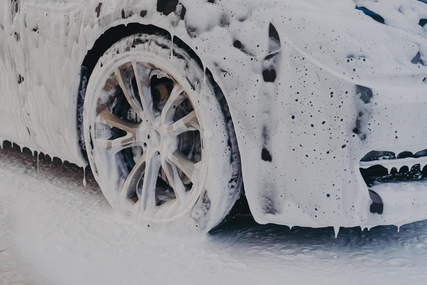 Car wheel in white soap foam at carwashing service station photo