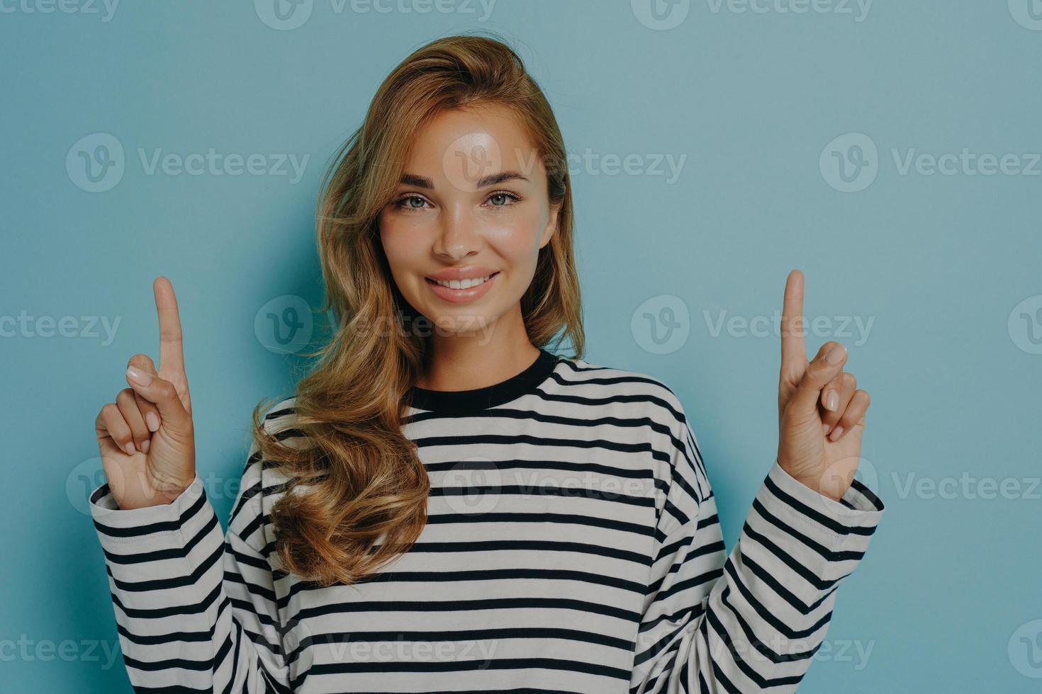 Photo of lovely smiling young woman points fingers up shows promo logo overhead