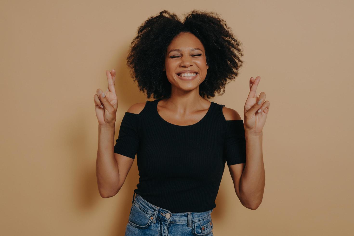 Cute lovely african american woman posing in casual clothes while gesturing fingers crossed sign photo