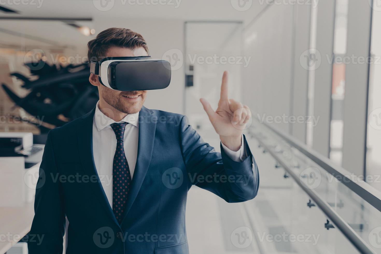 Smiling business professional in suit wearing VR headset on head using virtual reality at workplace photo