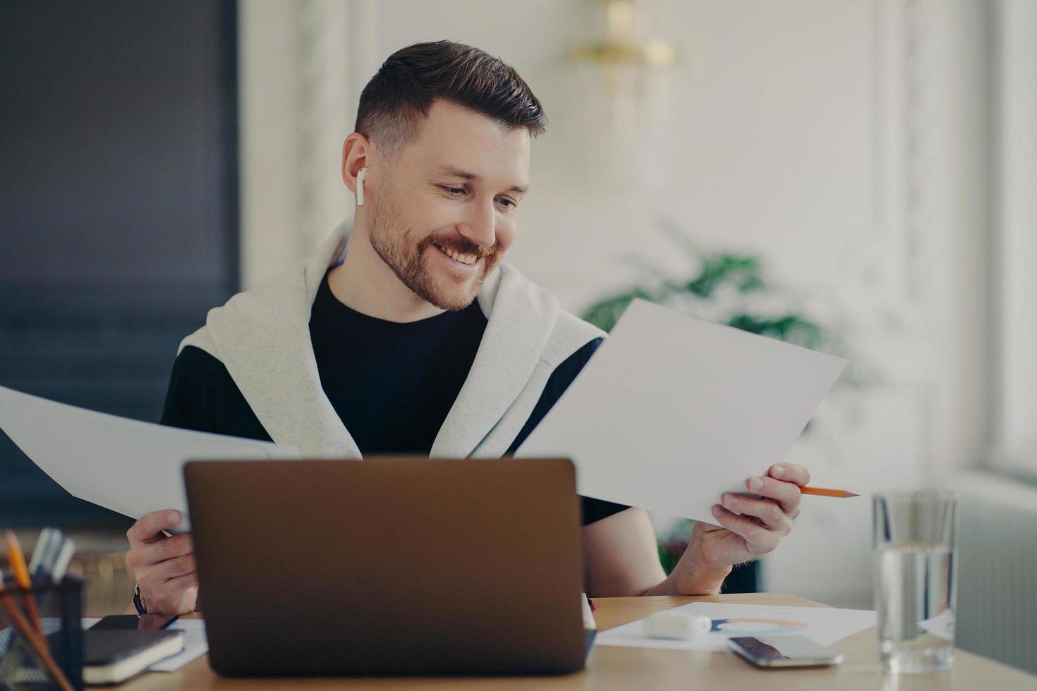 Handsome happy businessman analyzing documents and feeling satisfied while working on laptop from home photo