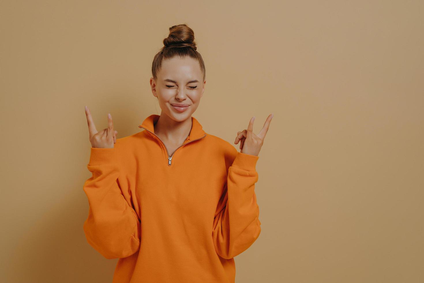 Overjoyed young woman showing rock-n-roll gesture, celebrating achievement with closed eyes photo