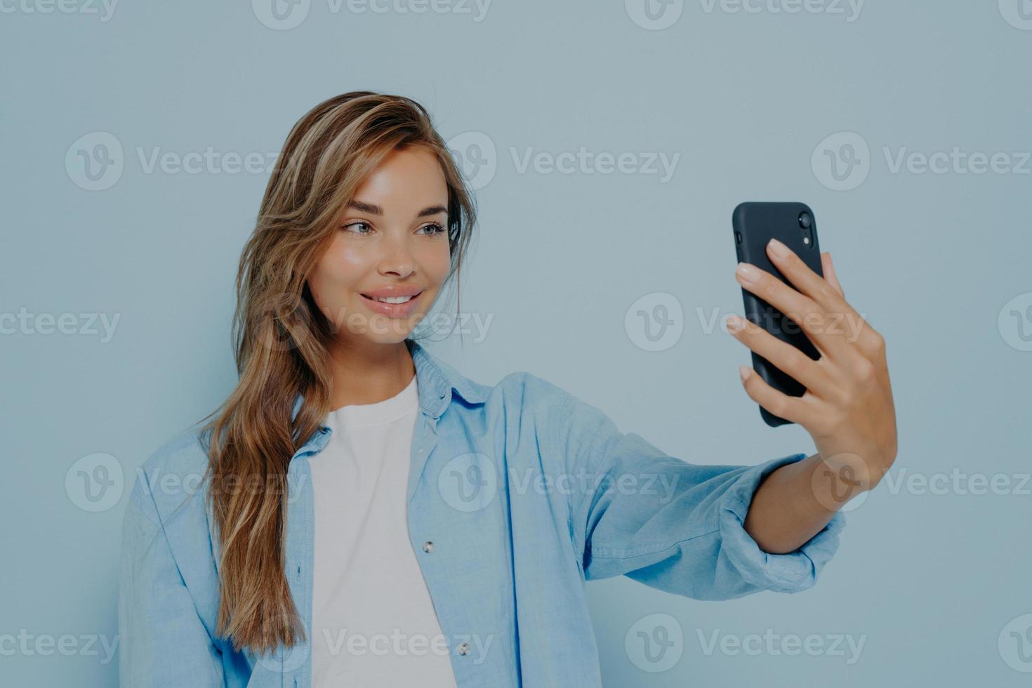 Beautiful woman taking photo of herself on light blue background