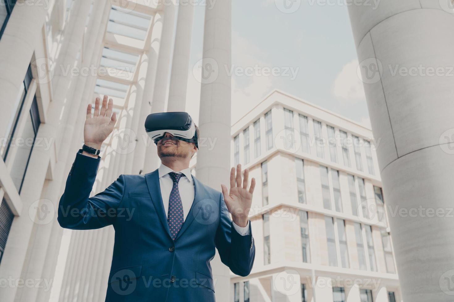 Futuristic image of happy businessman using virtual reality 3d goggles while standing outdoors photo