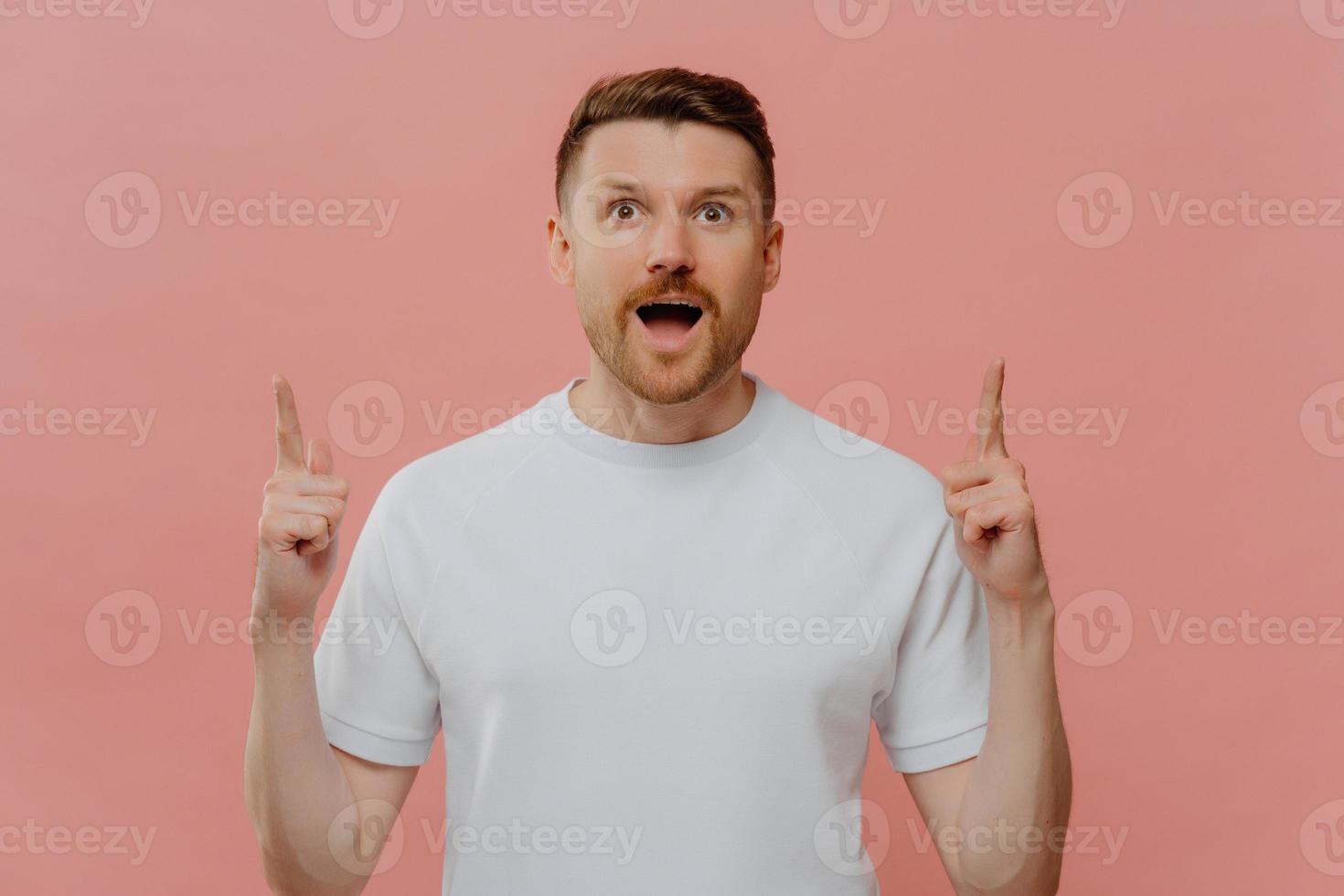 Excited young man pointing with two forefingers up and with shocked face expression photo