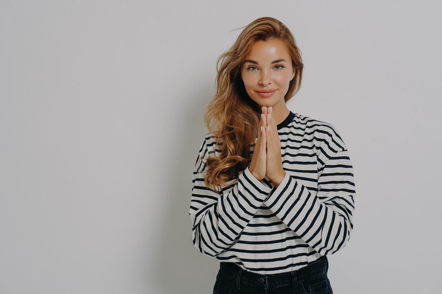 Pleading young blonde woman girl in casual striped shirt holding hands folded in praying gesture photo