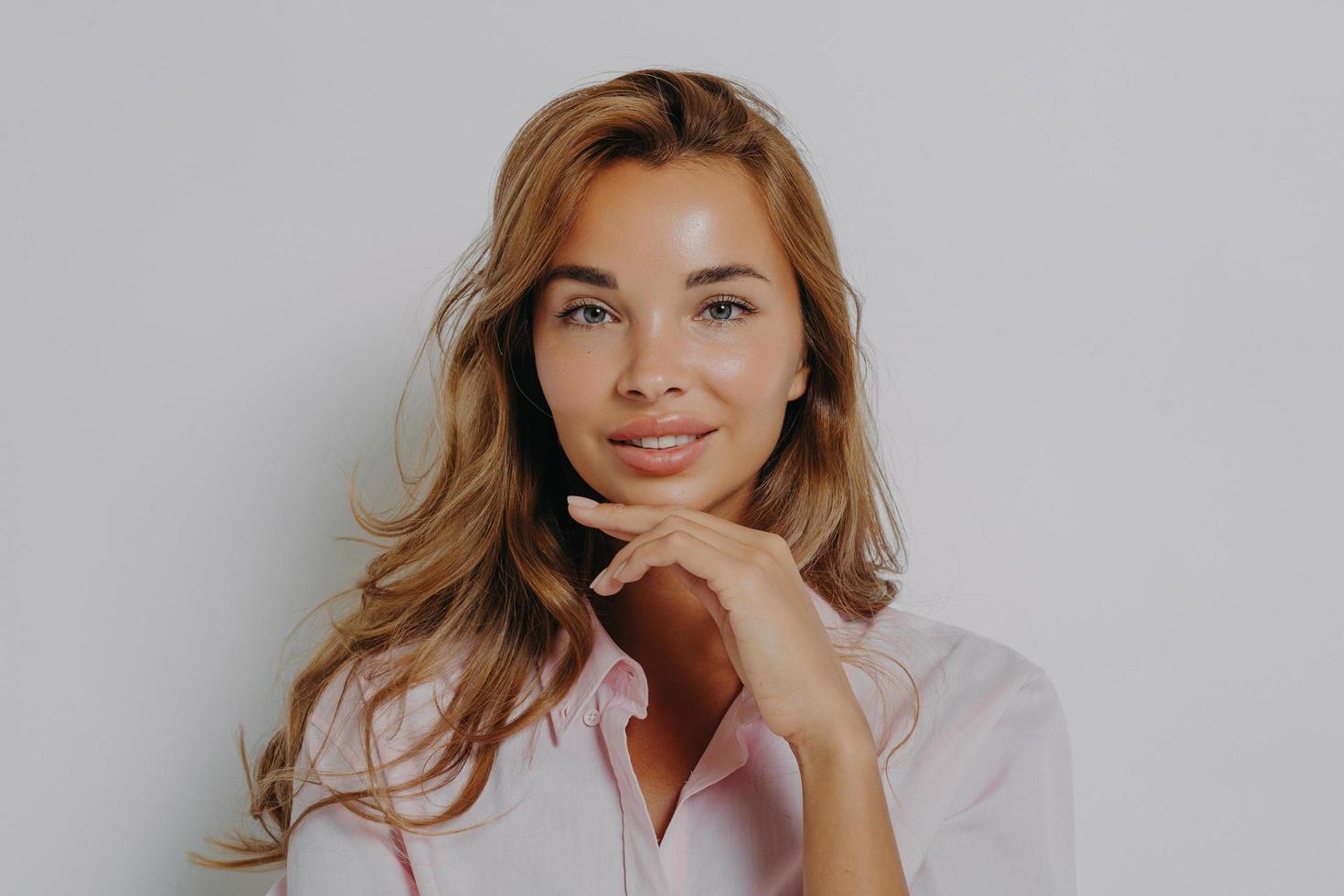 Portrait of good looking woman with long hair healthy skin minimal makeup touches chin gently photo