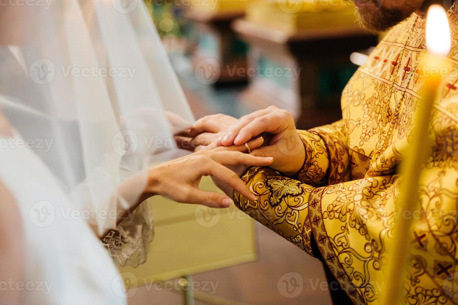 vista del sacerdote puesto en el anillo en la mano de la novia, pose en la iglesia cristiana durante la ceremonia de la boda, quemando velas en primer plano foto