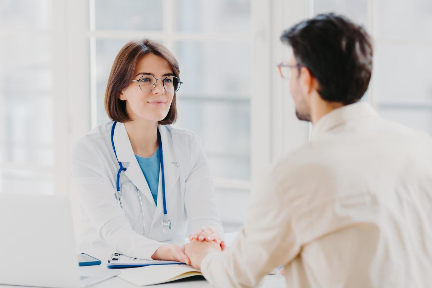 el paciente varón tiene consulta con una doctora, recibe apoyo, se entera de una enfermedad grave. mujer terapeuta consuela a un visitante enfermo en la oficina o en la sala de consulta, habla sobre cómo curar la enfermedad foto