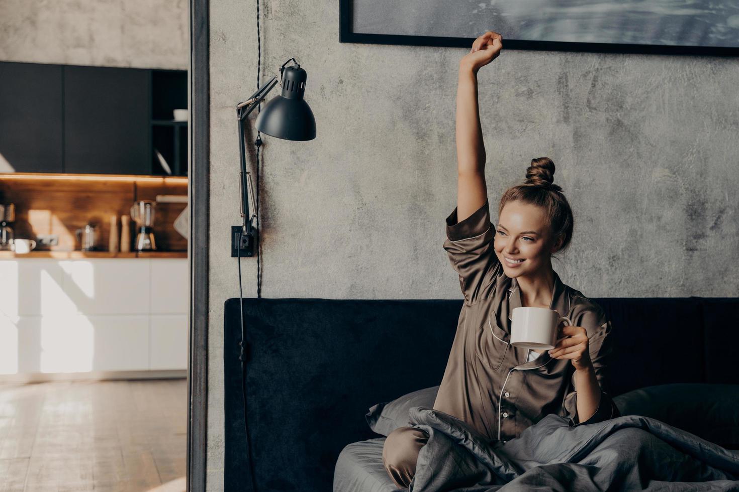 Attractive young happy female having morning coffee in bed photo