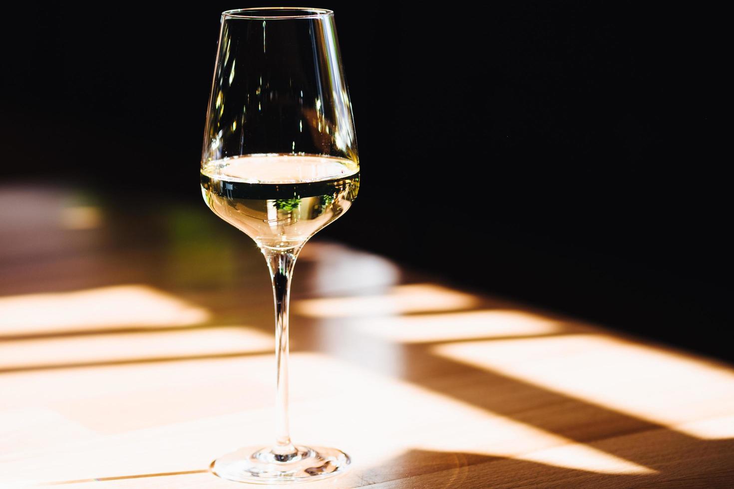 Shot of glass of white wine stands on table in restaurant. Alcoholic drink in cafe on bar counter. Drink in glass on wooden desk. Celebration concept. photo