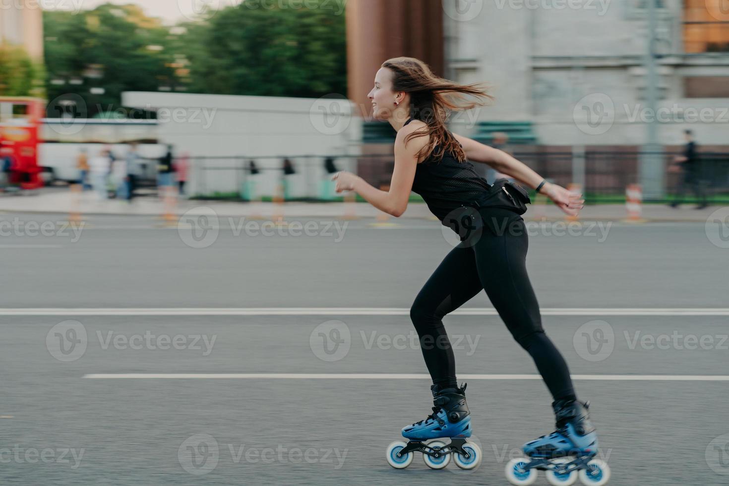 Active leisure concept. Full length shot of young slim woman rollerblades along asphalt on street enjoys speed spends free time on favorite hobby poses outdoors breathes fresh air. Rollerskating photo