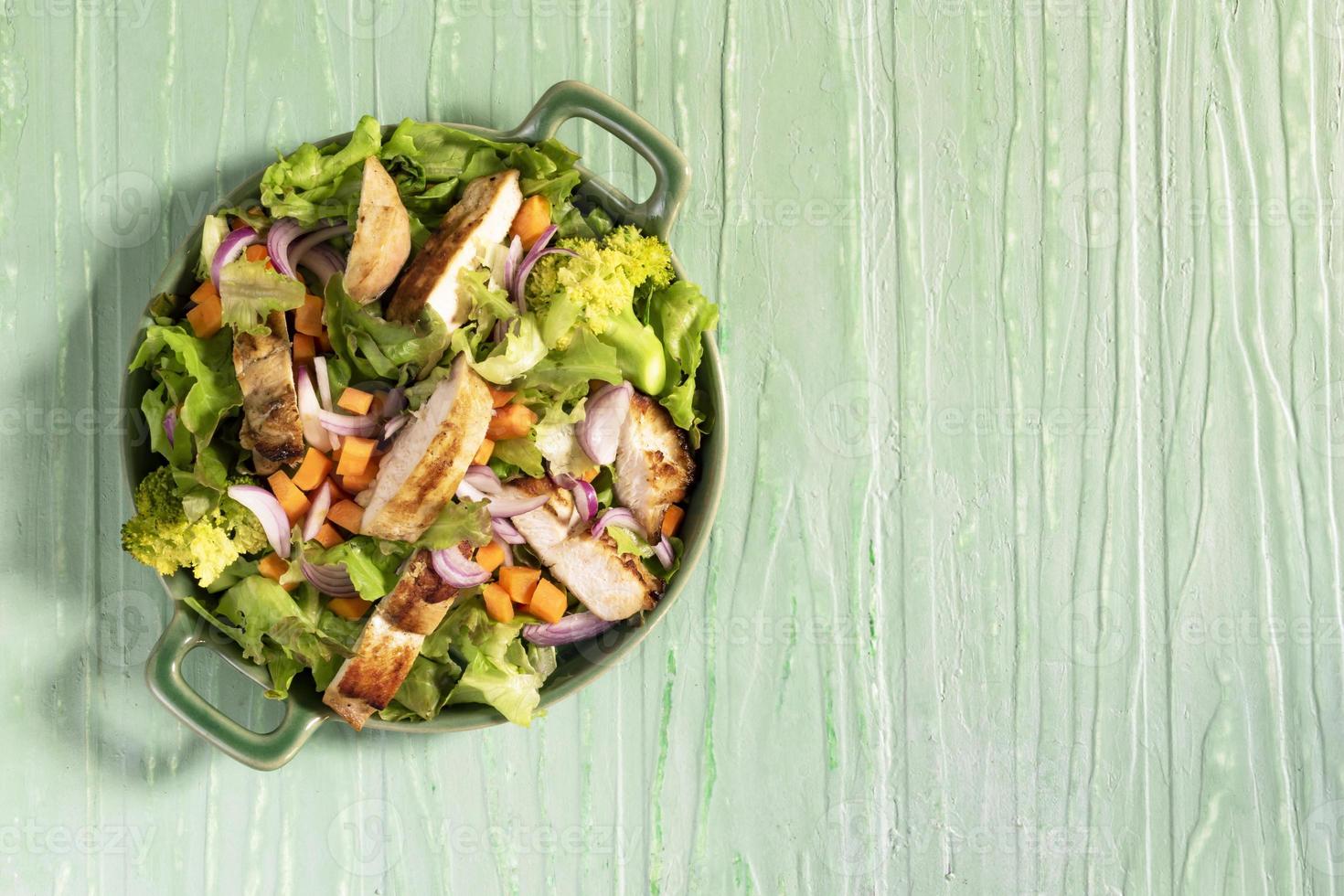 Healthy food salad bowl has chicken carrot broccoli on green wood table. photo