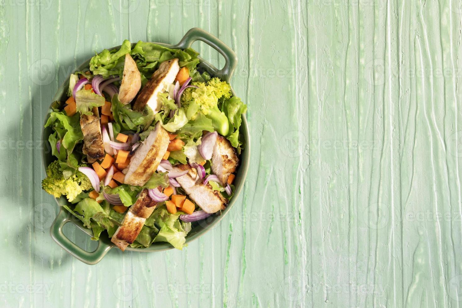 la ensaladera de comida saludable tiene brócoli de pollo y zanahoria en una mesa de madera verde. foto