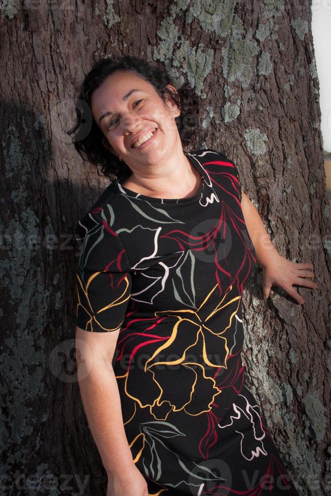 señora madura en el parque en un día soleado disfrutando de pie contra un árbol. foto