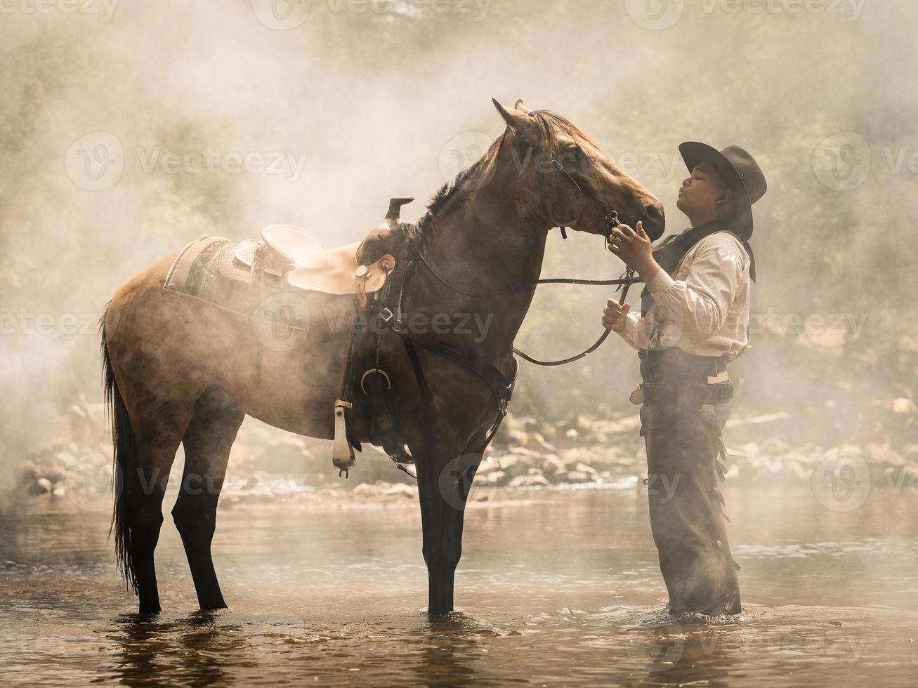 un joven vaquero descansó con un caballo en el arroyo después de que terminó de duchar al caballo foto