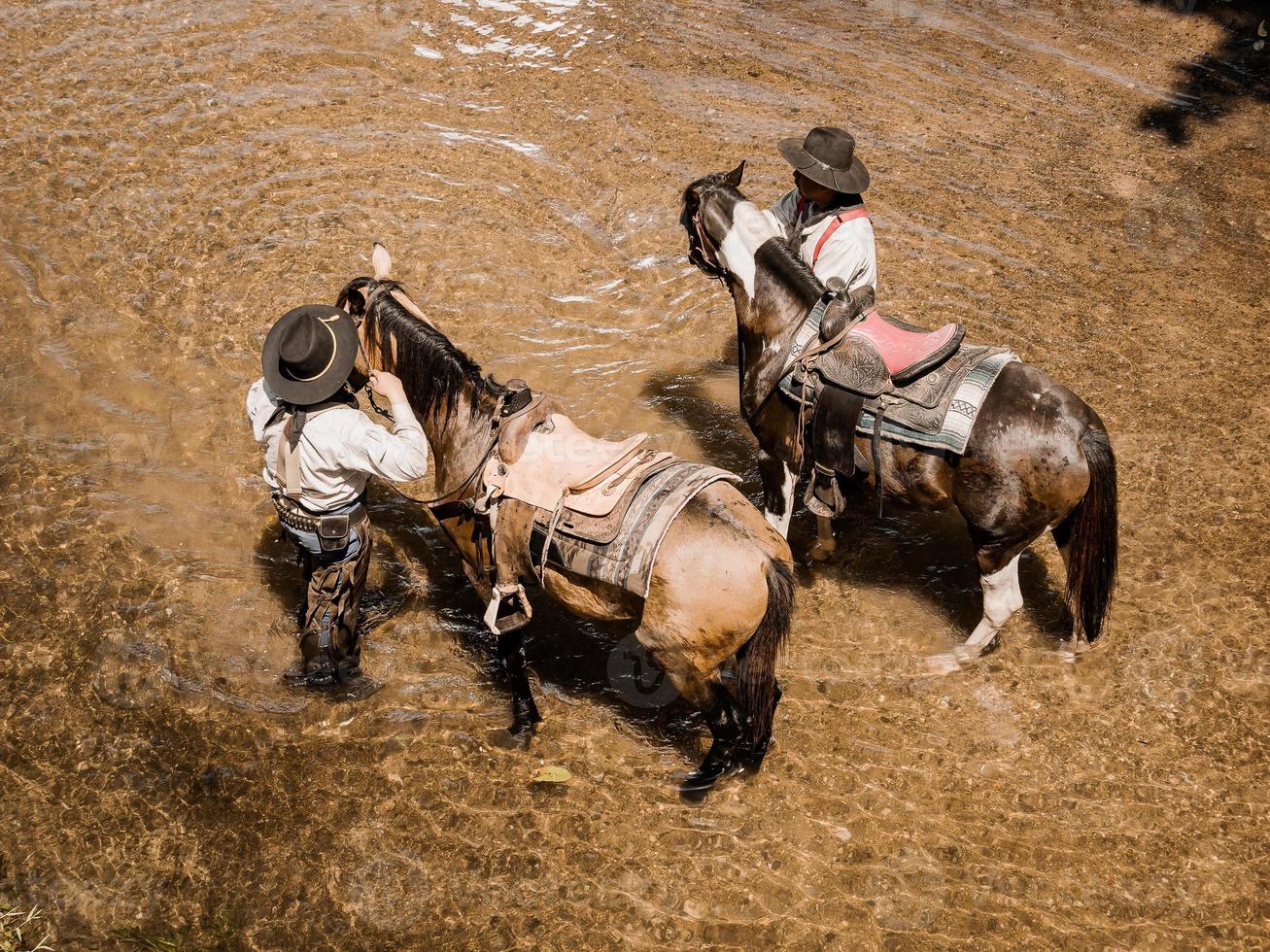 viejos y jóvenes vaqueros descansan con sus caballos en el arroyo después de terminar de bañarse foto