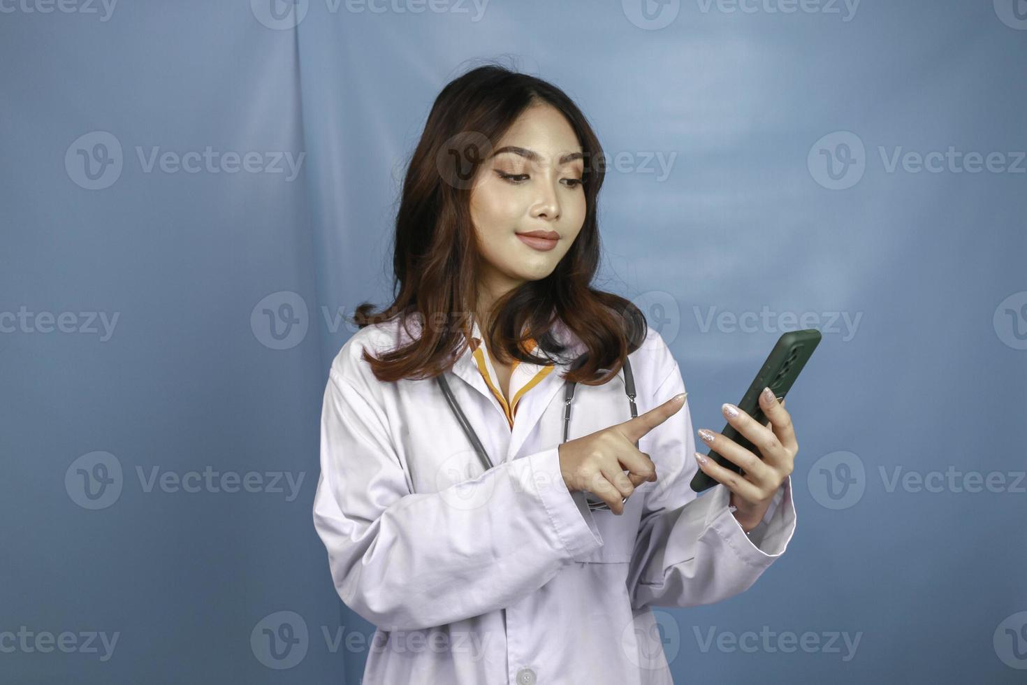 Young Asian woman doctor is pointing and showing green screen or copy space on her smartphone photo