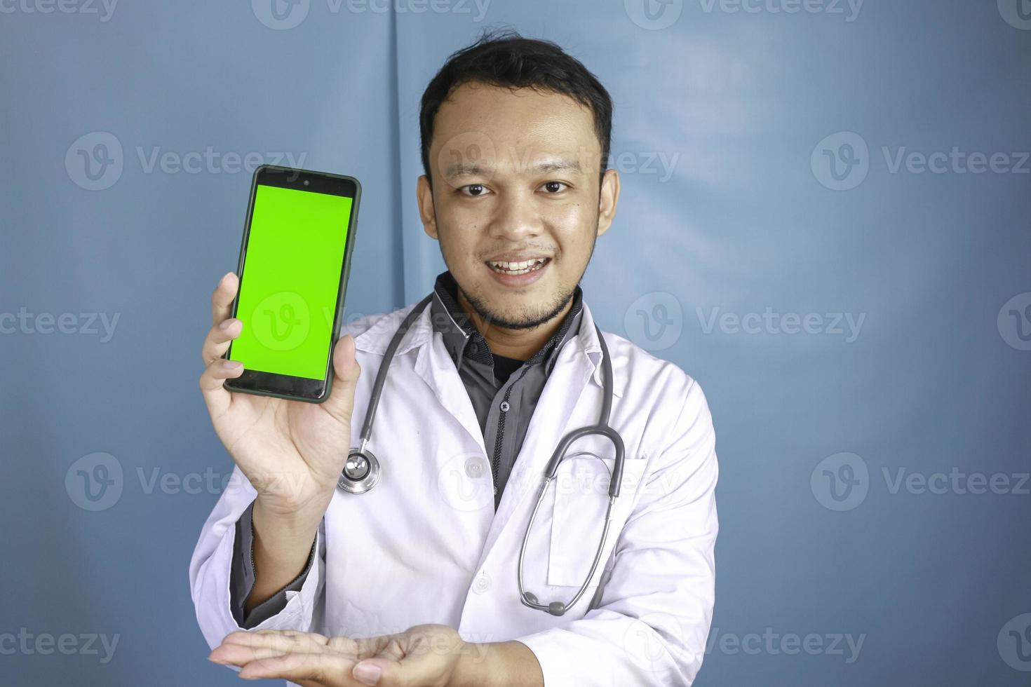 Young Asian man doctor is showing green screen or copy space on his smartphone photo