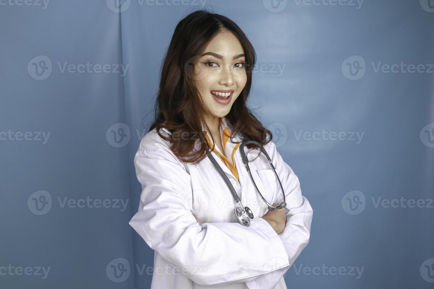 Portrait of an attractive confident female doctor, friendly smiling arms crossed wear white lab coat stethoscope isolated blue color background photo