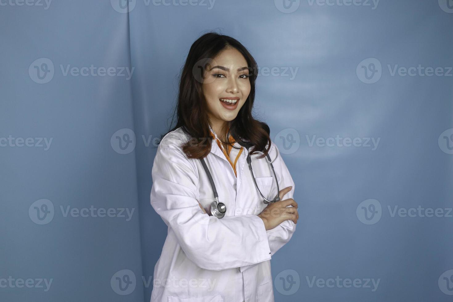 Portrait of an attractive confident female doctor, friendly smiling arms crossed wear white lab coat stethoscope isolated blue color background photo