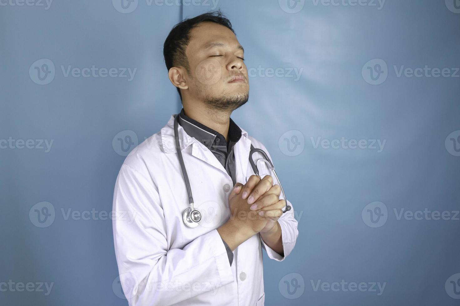 A portrait of a young Asian male doctor is praying to God photo