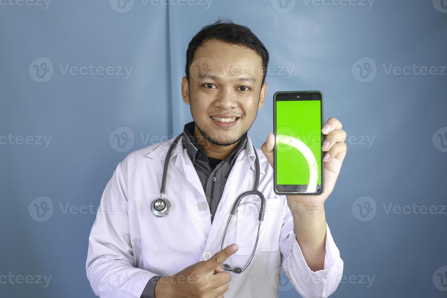 Young Asian man doctor is showing green screen or copy space on his smartphone photo