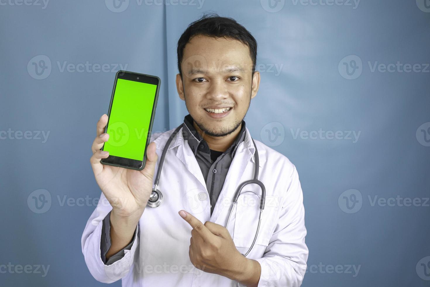 Young Asian man doctor is showing green screen or copy space on his smartphone photo