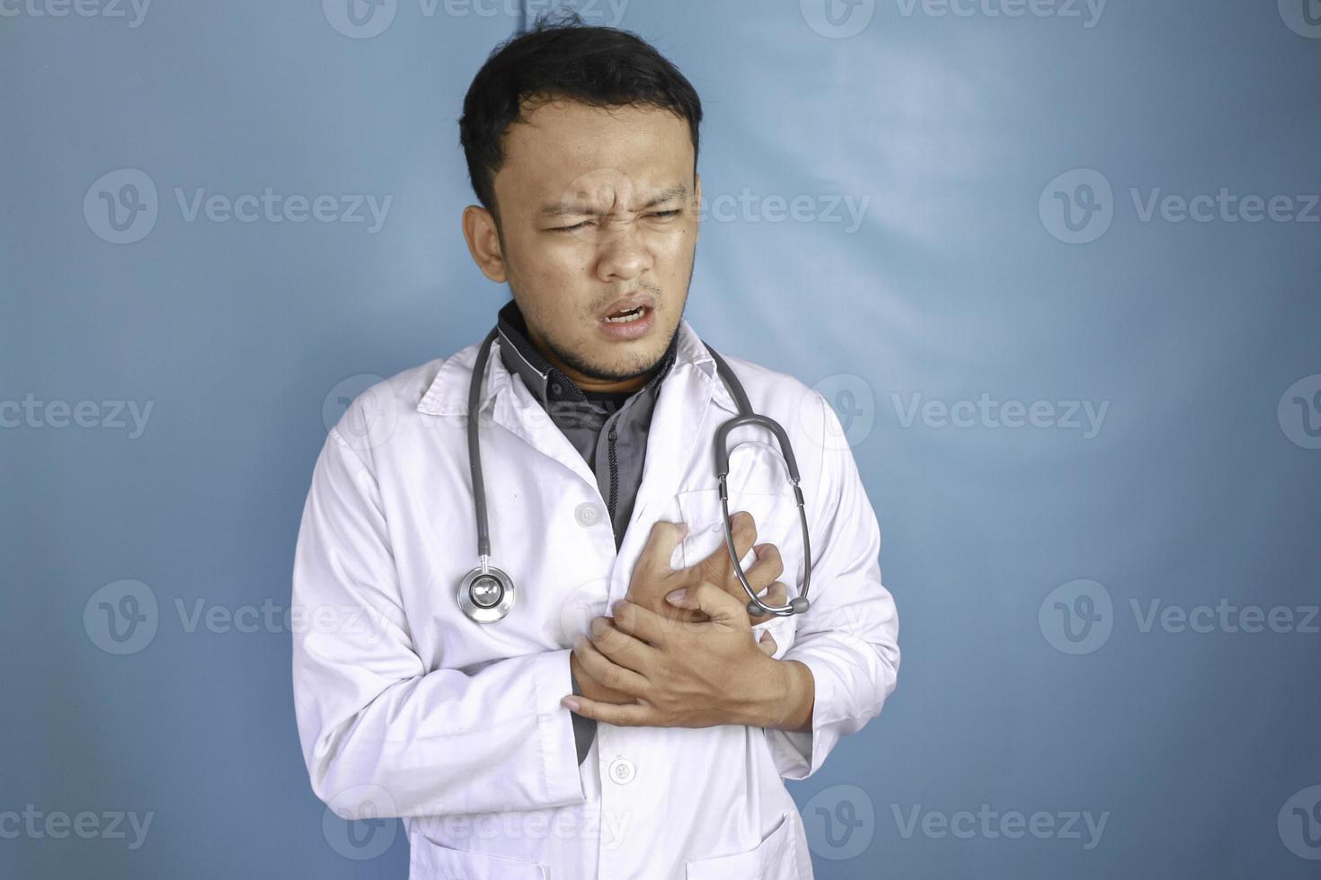 A portrait of a young Asian male doctor looks in pain on his chest photo