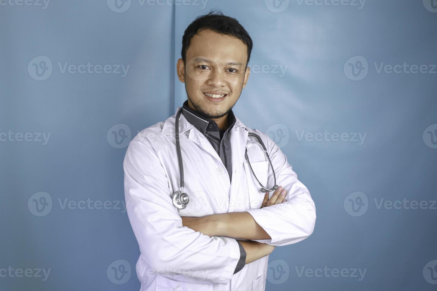 Portrait of an attractive confident male doctor, friendly smiling arms crossed wear white lab coat stethoscope isolated blue color background photo