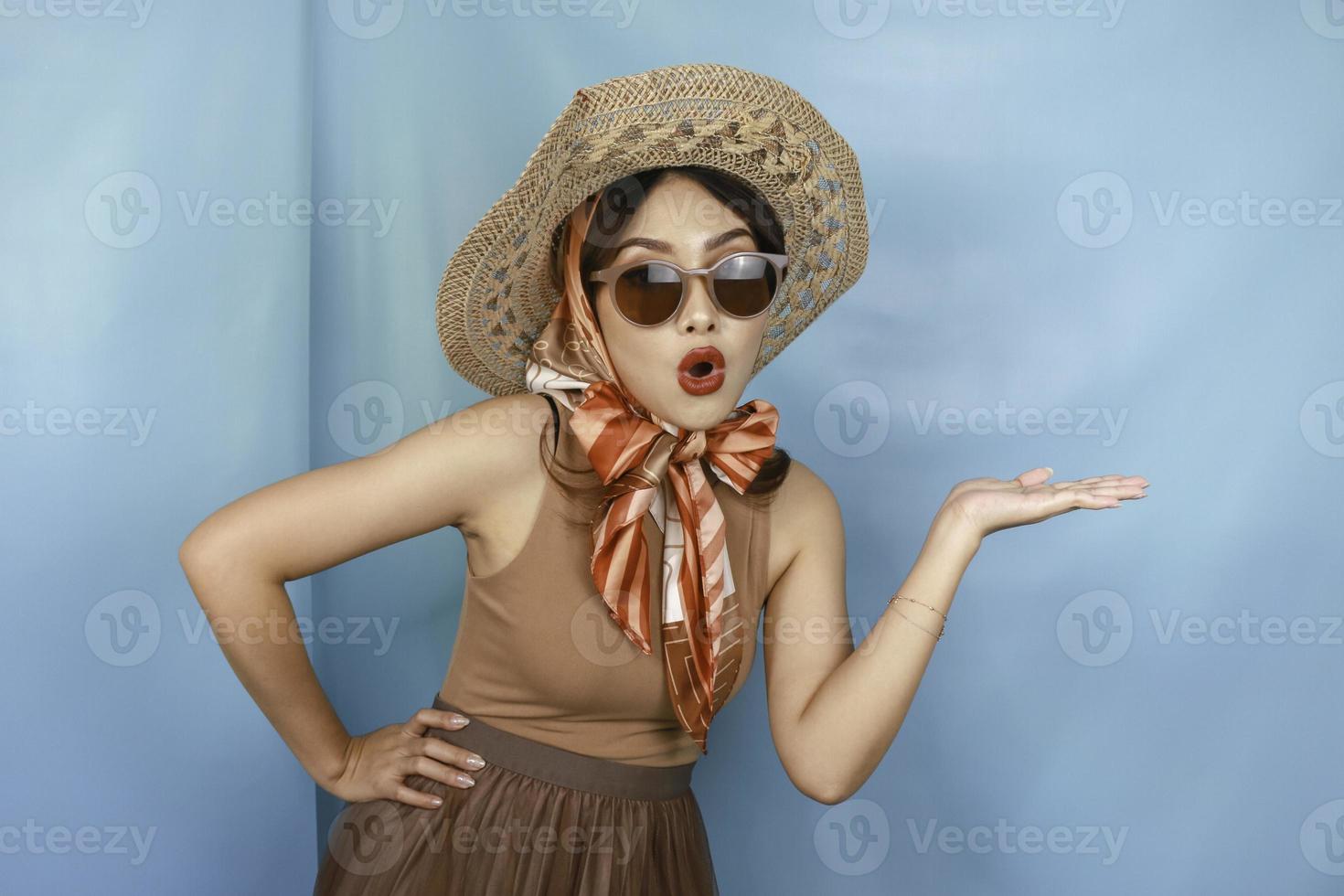 Young Asian shocked woman isolated by a blue background pointing copy space on the side. photo