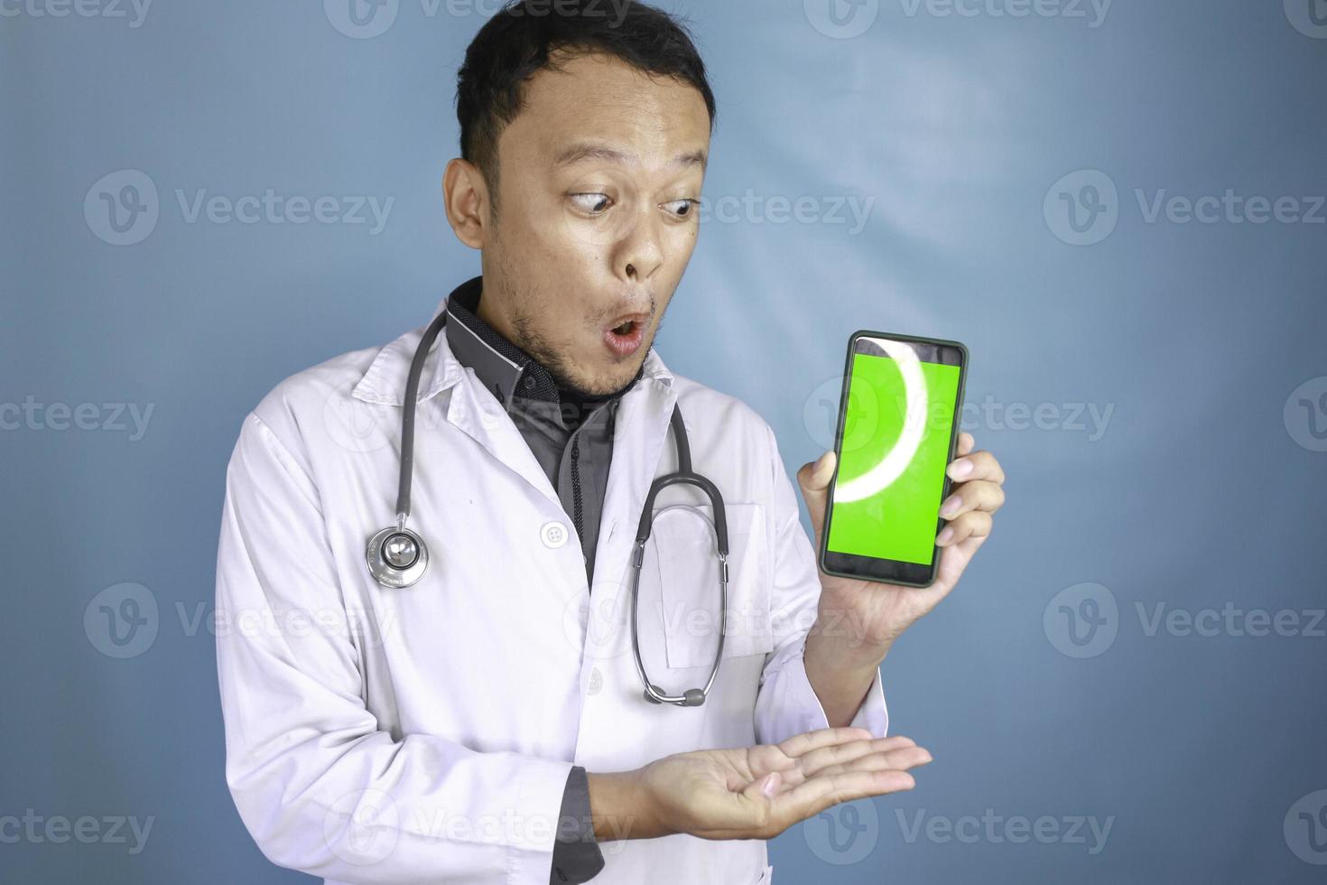 Young Asian man doctor is showing green screen or copy space on his smartphone photo