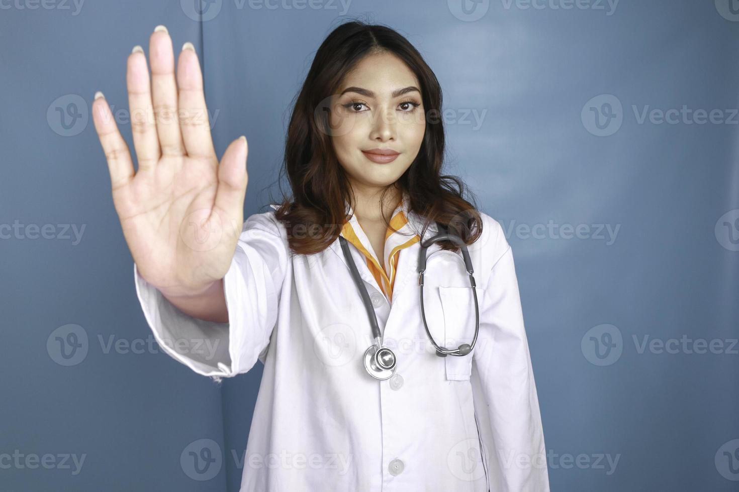 Serious Asian female doctor with stethoscope and white coat, showing stop sign. photo