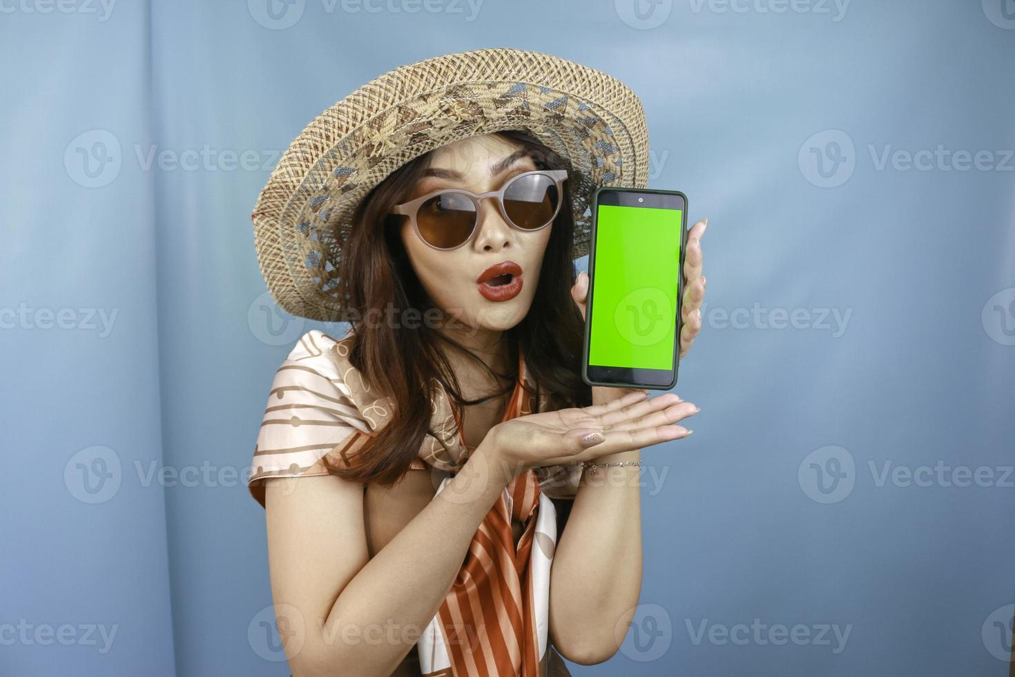 Young Asian happy woman showing and shocking to her smartphone isolated by a blue background photo