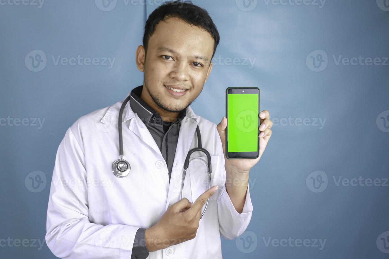 Young Asian man doctor is showing green screen or copy space on his smartphone photo