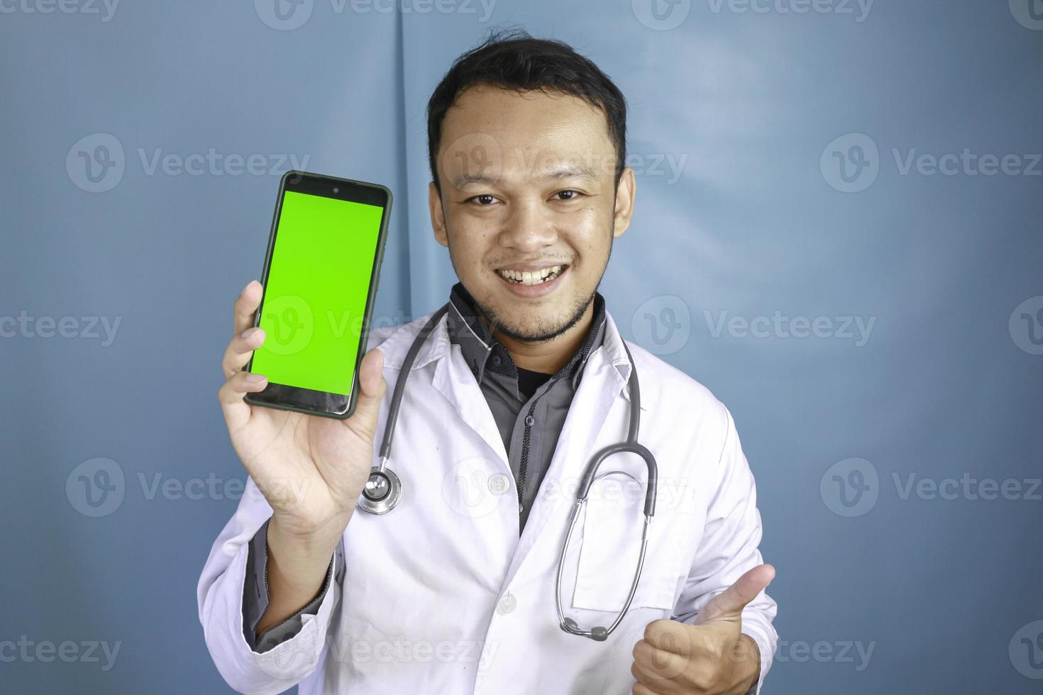 Young Asian man doctor is showing green screen or copy space on his smartphone photo