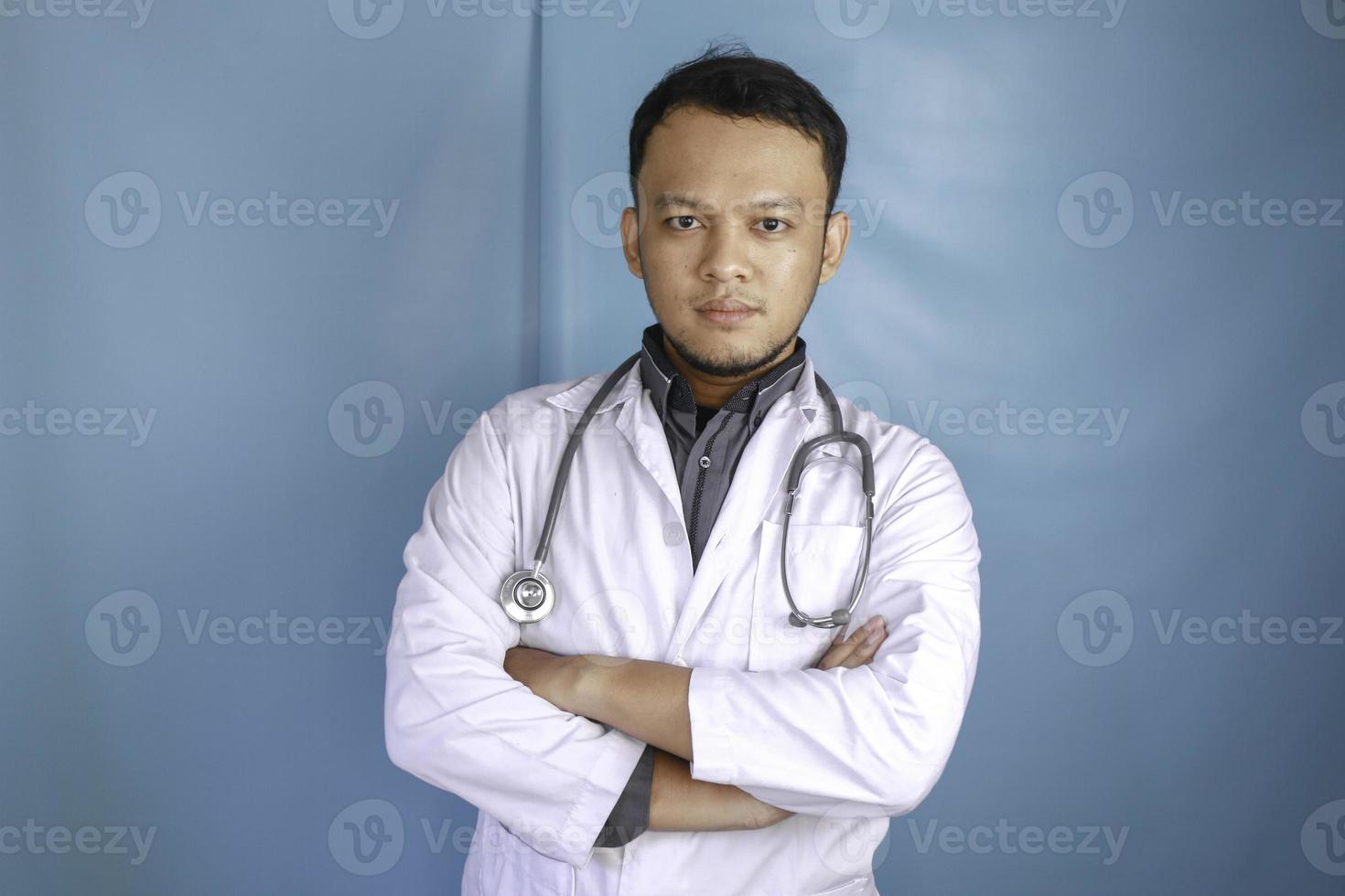 Portrait of an attractive confident male doctor, friendly smiling arms crossed wear white lab coat stethoscope isolated blue color background photo