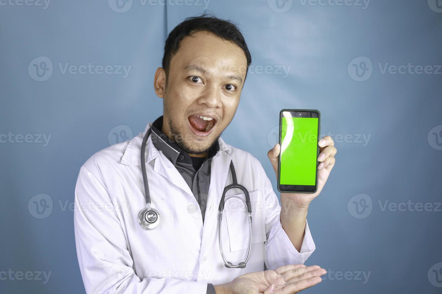 Young Asian man doctor is showing green screen or copy space on his smartphone photo