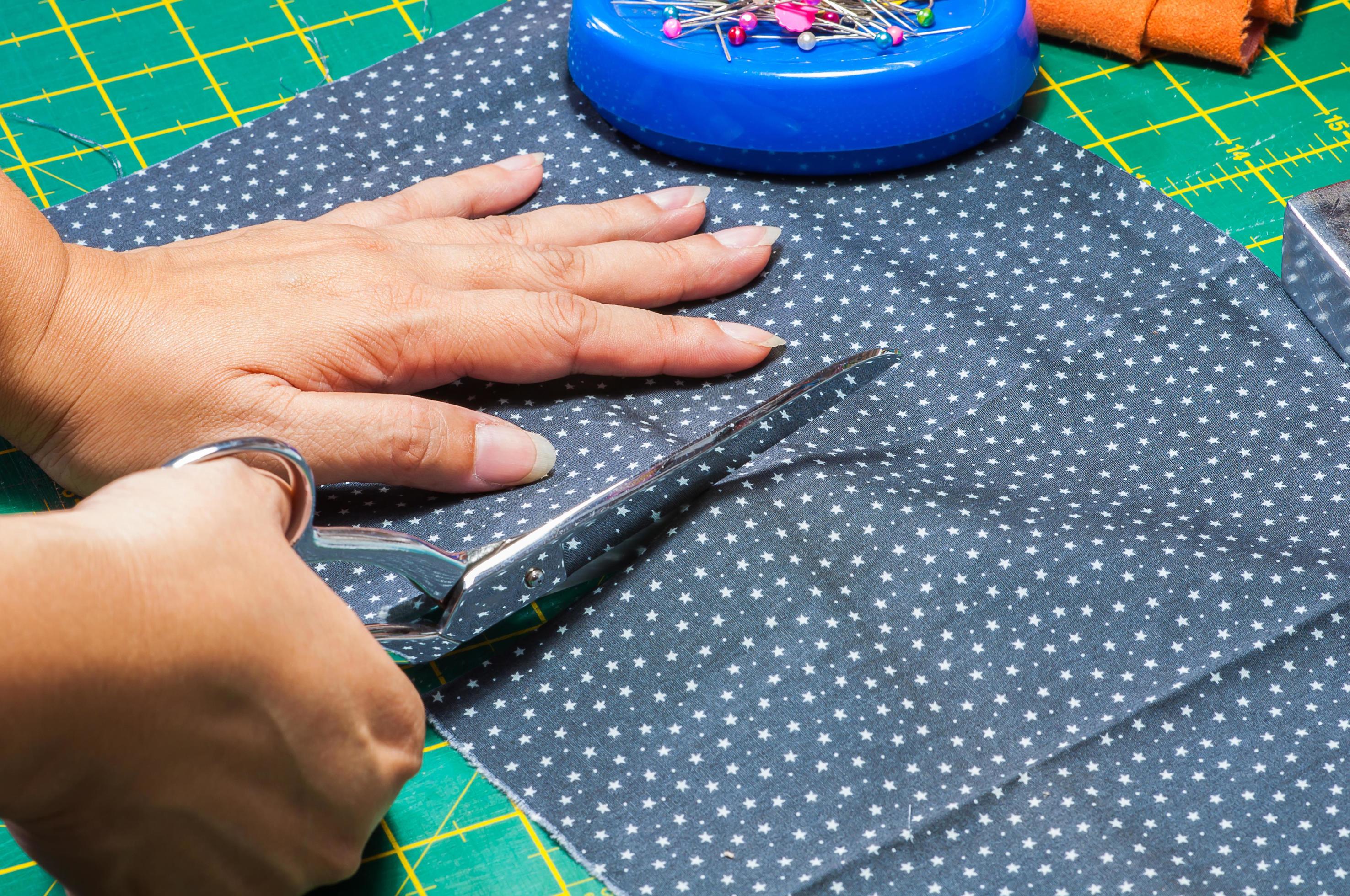 Woman's hands, doing her patchwork using scissor cutting cloth 8860473