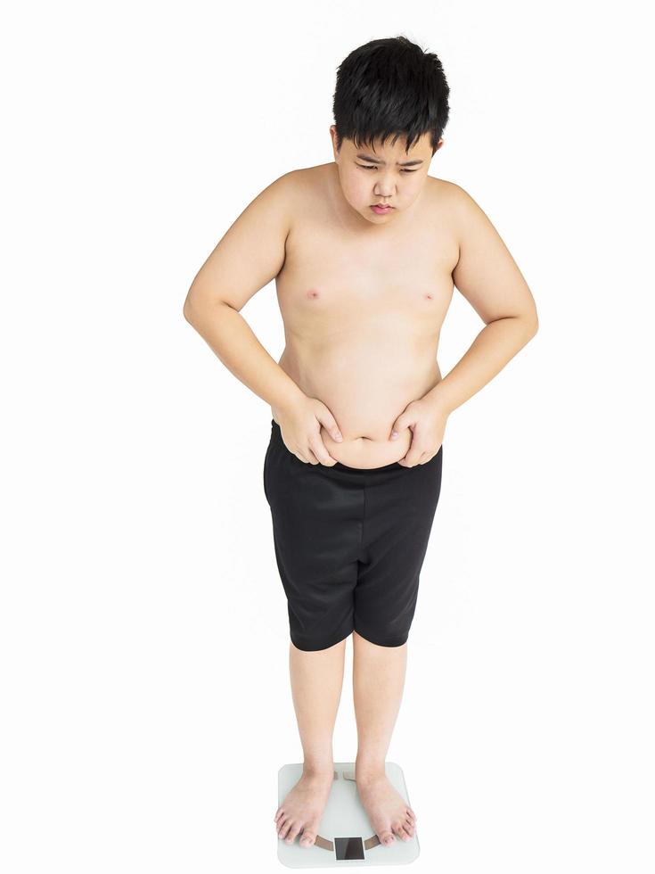 Soft focus of fat boy disappoint his fatness while standing on on weighing machine over white background photo