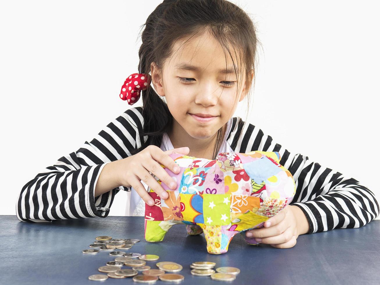 Asian kid is putting money in to a colorful piggy coin bank photo
