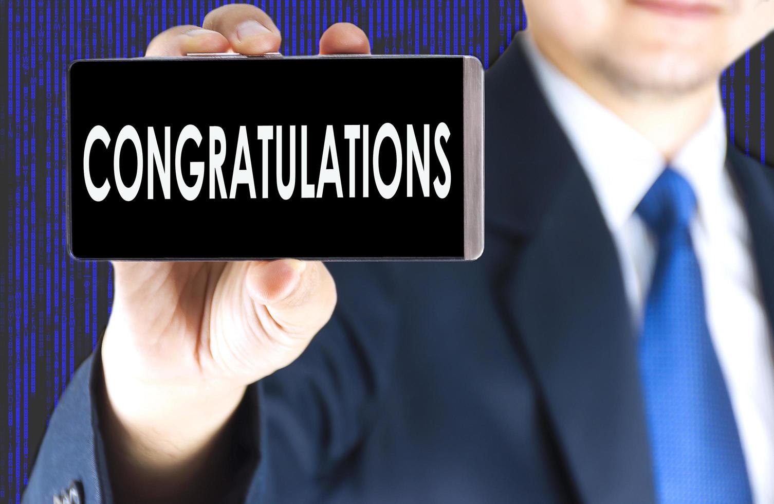 Focused of congratulations word on mobile phone screen in blurred young businessman hand and digital technology background photo