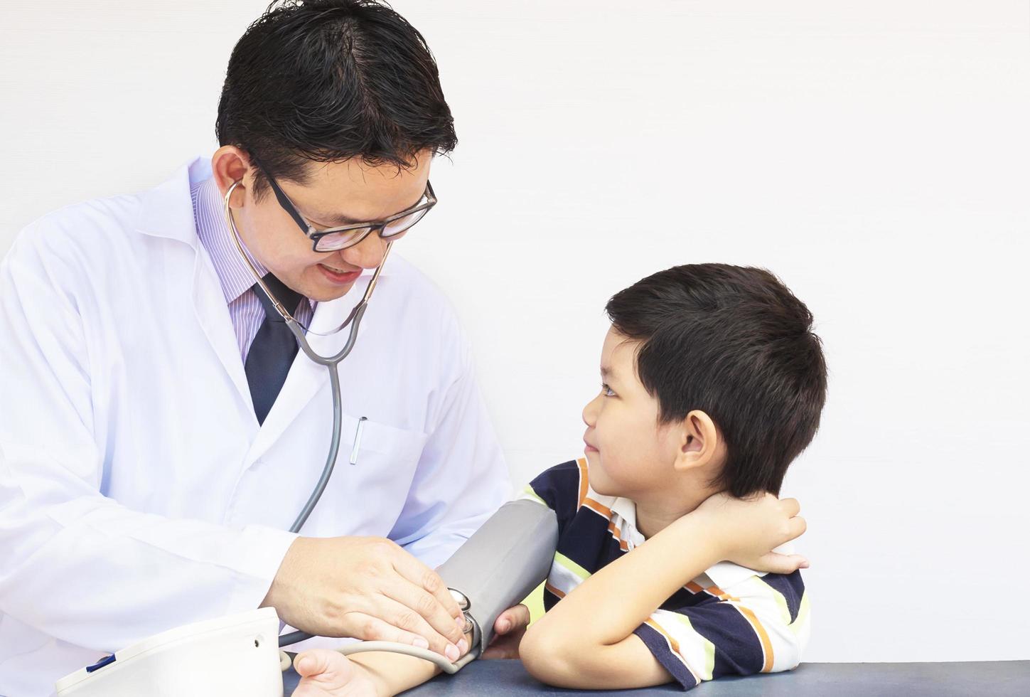 Asian boy being examined by male doctor using stethoscope and blood pressure monitor over white background photo