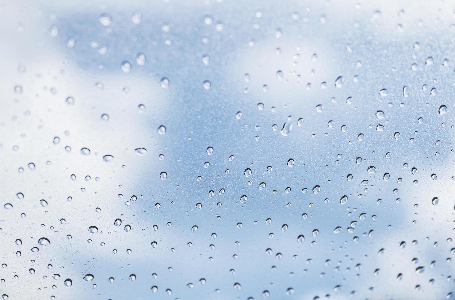 Rain drop on at glass window over blue sky background photo